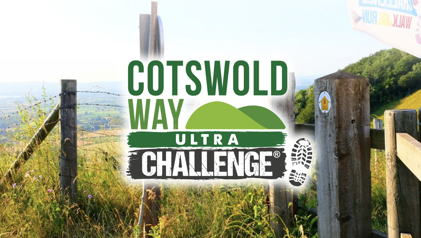 Beautiful countryside view along the Cotswold Way, featuring a wooden gate and signpost surrounded by tall grass and wildflowers. Rolling hills stretch into the distance under a clear sky. The Cotswold Way Ultra Challenge logo is prominently displayed over the image.