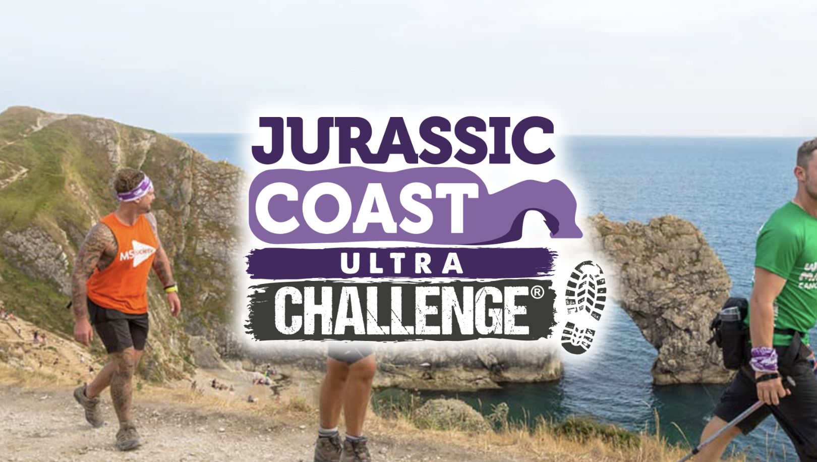 A promotional graphic for the "Jurassic Coast Ultra Challenge," featuring bold purple text with a dinosaur silhouette integrated into the design. The background shows participants walking along a dramatic coastal trail with the iconic Durdle Door rock formation and the sea visible in the distance. The rugged cliffs and blue skies highlight the natural beauty of the route. Boot print graphics at the bottom of the logo emphasise the adventurous and active nature of the challenge.