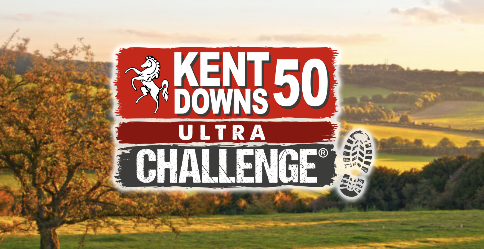 A stunning countryside scene at sunset, showcasing the rolling hills of Kent Downs with trees and fields bathed in warm golden light. The event logo, featuring the words "Kent Downs 50 Ultra Challenge" with a white horse emblem and a boot print, is prominently overlaid on the image. The peaceful rural landscape creates a sense of adventure and natural beauty.