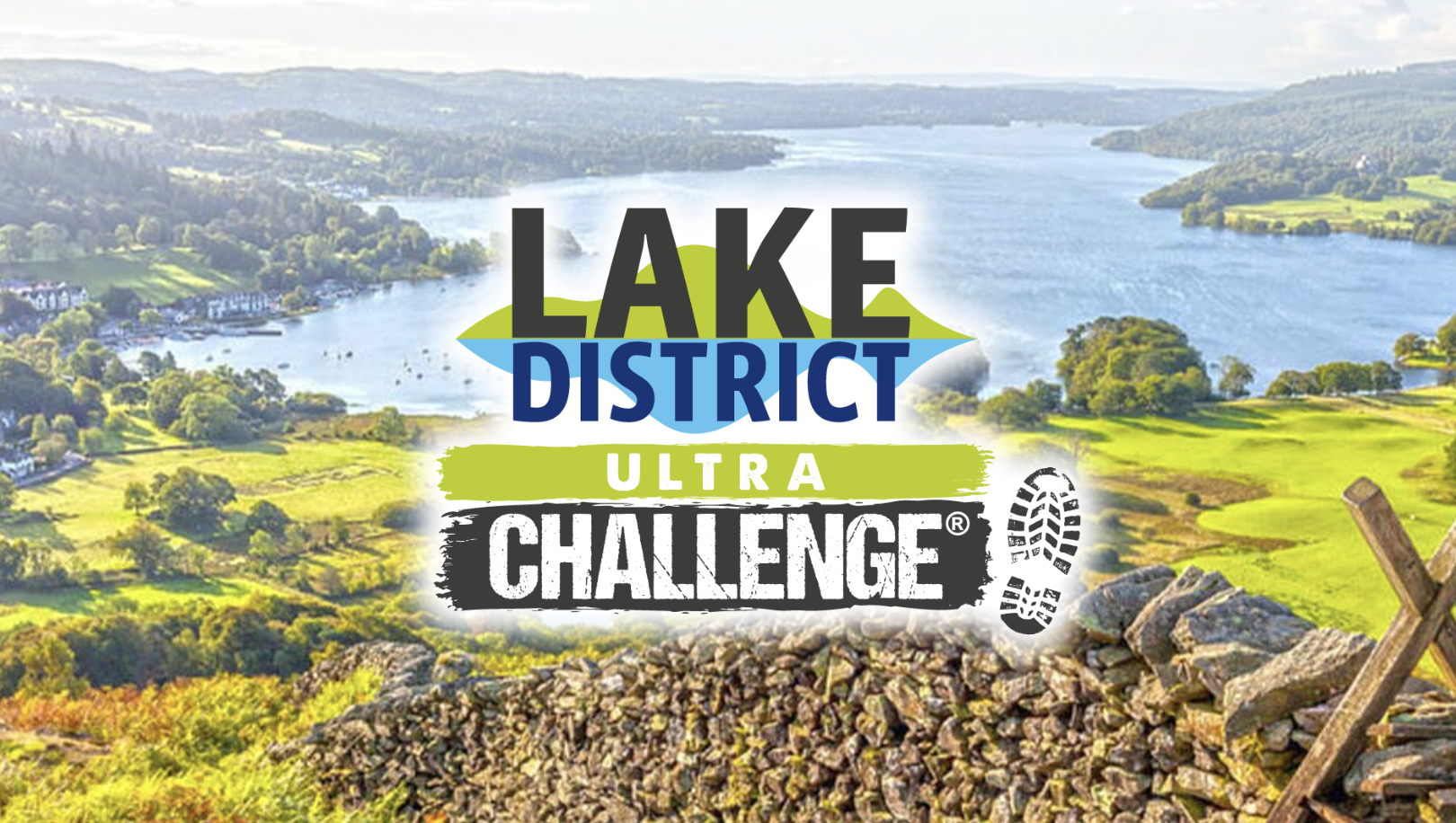 Scenic view of the Lake District featuring lush green fields, a stone wall in the foreground, and a tranquil lake surrounded by rolling hills under a bright sky. The Lake District Ultra Challenge logo is prominently displayed over the image.